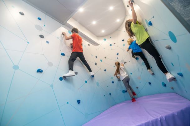 Niños practicando escalada en pared infantil con colchonetas de gimnasio de seguridad en el suelo